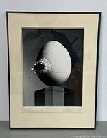 Framed surrealist photograph showing the entire artwork with black frame and cream matte, artwork depicting a cracked egg on a clear pedestal.