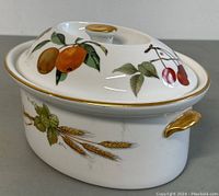 Side angle view of the tureen showing orange and cherry fruit detail with gold accents on lid knob and handle.