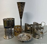 Full set of items on a table: three pewter Russian tea glass holders missing inserts, silver plated goblet, coffee canister made in India, small silver decorative dish. Shows wear and tarnish.