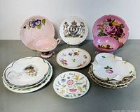Multiple assorted tea cups and saucers including pink floral, regal crest and scalloped edges