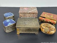 Full view of six trinket boxes including metal, enamel, composite, and stone materials.