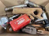 Box of assorted vintage tools including wooden hand planes, flashlights, metal scoop, wrench, wooden mallet, and other hand tools.