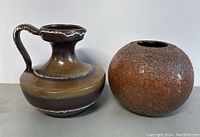 Front view of West German Cullmann ceramic pitcher and hand-made rounded vase positioned side by side on a white surface against a plain background. Shows smooth glaze on pitcher and rough textured surface on vase.