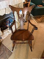 Full front view of the antique wooden rocking chair showing carved backrest, armrests and seat.