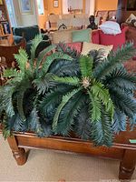 Top view showing the full artificial fern plant with thick, lush green fronds spread widely across a wooden surface.