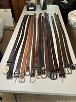 Full view of the 11 leather belts laid out on table showing variety of buckle styles and colors