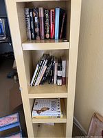Books arranged on three shelves of a yellow bookcase. Lower shelves have various books on hunting, birds, and nature.