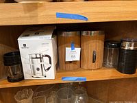 Shelf with Nespresso Aeroccino box, coffee grinder vessel, and wood grain canisters labeled sugar and flour with metal lids and a black electric frother