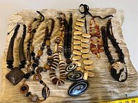 Full view of all eight chunky necklaces laid flat on fabric showing variety of bead shapes, materials, and tones.