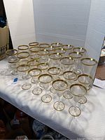 Full set of 26 clear glasses with gold rims arranged on a table.