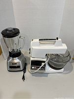 Full view of Oster mixer with glass bowl and Oster blender with glass jar and black lid on white surface with plain background.