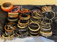 Top-down image showing a large collection of bracelets stacked and arranged together including wood, metal, beaded, plastic, and animal print designs.