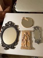 Lot display showing all four items on a white table including three decorative mirrors and one carved plaque.