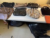 Table with nine assorted purses in various styles, materials, and colors including quilted bronze tote, hobo styles, black and zebra print bags