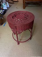 Red metal table showing ornate top and leg design