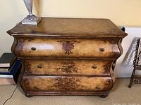 Front view of painted wooden dresser showing floral designs and curvy front shape.