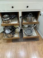 Open cupboard with four sliding drawers containing various pots, pans, and kitchen strainers, showing the layout and quantity.