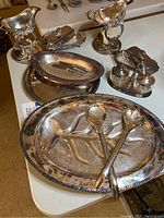 Full assortment of silver plated serving pieces on a table including gravy boats, platters, jam container, butter dishes, salt and pepper shakers, and utensils.