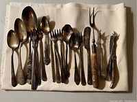 All utensils arranged on a cream cloth, showing variety of spoons, forks, and two larger serving forks with wooden handles