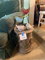 Photo of the round resin stand topped with four bird figurines on a carpeted floor next to a green chair.