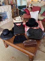Photo showing three vintage hats, three purses, and two hat boxes arranged on a wooden table and couch in a room.