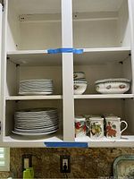 Kitchen cabinet with stacked small plates, large plates, bowls, and coffee mugs.