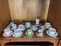 View of entire lot of eleven assorted fine bone china tea cups with saucers showing variety of floral patterns and colors.