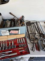 Photo of socket set, hand tools in bin, some saws, and a metal clipboard on a table