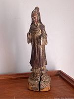 Full front view of the standing Kwan Yin wooden statue on a wooden surface showing entire figure and base with crack.