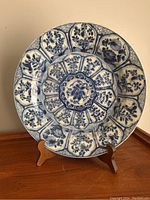 Front view of a 17th century Chinese blue and white porcelain plate on a wooden stand with floral and botanical hand-painted pattern.