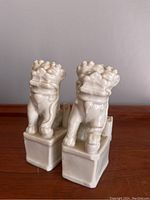 Front view of two white glazed ceramic Foo Dog figurines on square bases showing detailed features and size.