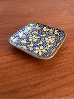 Photo showing top angle of tiny square enamel tray with blue background and yellow floral pattern.