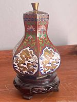 Full view of the Chinese enamel ware bottle on the carved wooden stand showing the red background and detailed colorful dragon and floral enamel designs.