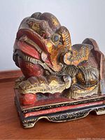 Close view of the Foo Dog's head showing red and gold paint with detailed carved teeth and eyes, displaying vintage wear.