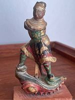 Side angle showing front and left side of the Asian gilt wooden carving figurine standing on wave base with red, green, and gold painted details.