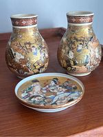 Photo showing two small Satsuma vases with detailed hand-painted traditional Japanese figures, floral patterns, and gold accents, alongside a round Satsuma plate with painted figures.
