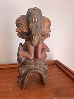 Rear view of the antique African wooden figure showing the second face, dual-face design, cowrie shell decorated headdress, and base support structure.