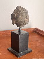 Photo showing side angle of stone Buddha head sculpture on black base.