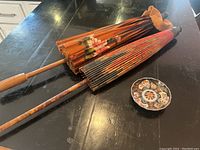 Photo showing two folded Asian parasols with painted floral patterns lying parallel on a black surface, with wooden handles and ribs.