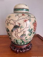 Front view of Chinese Republic period ginger jar with floral and bird designs on crackled glaze background, sitting on wooden stand.
