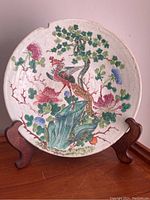 Full view of round porcelain plate with painted bird and floral design on wooden display stand.