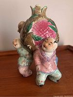 Front view of polychrome porcelain sculpture showing three children supporting peach vessel