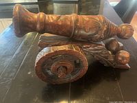 Wooden Witco carved cannon sculpture side view showing detailed wheel and barrel carvings on dark wood.