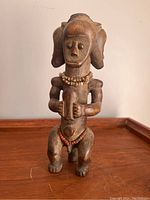 Front view of the wooden three-headed African figure standing upright on a wooden surface.
