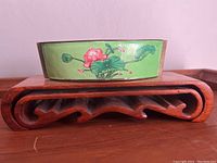 Side view of boat-shaped enamel dish with lotus flower decoration on wooden stand