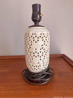 Full view of the porcelain lamp body on wooden surface with electrical socket and cord coiled at base.