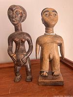 Two antique African wooden figurines standing side by side on wooden surface, showing front views with clear facial and body details.