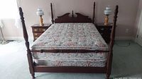 Full view of bed showing four wooden posts and mattress on bed frame.