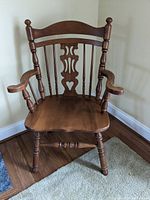 Front view of wooden captains chair showing decorative back with heart-shaped cutout, spindle arms, and turned legs.