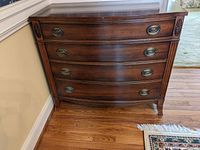 Front view of the chest showing curved drawer fronts, oval brass pulls, and carved floral accents on the corners.